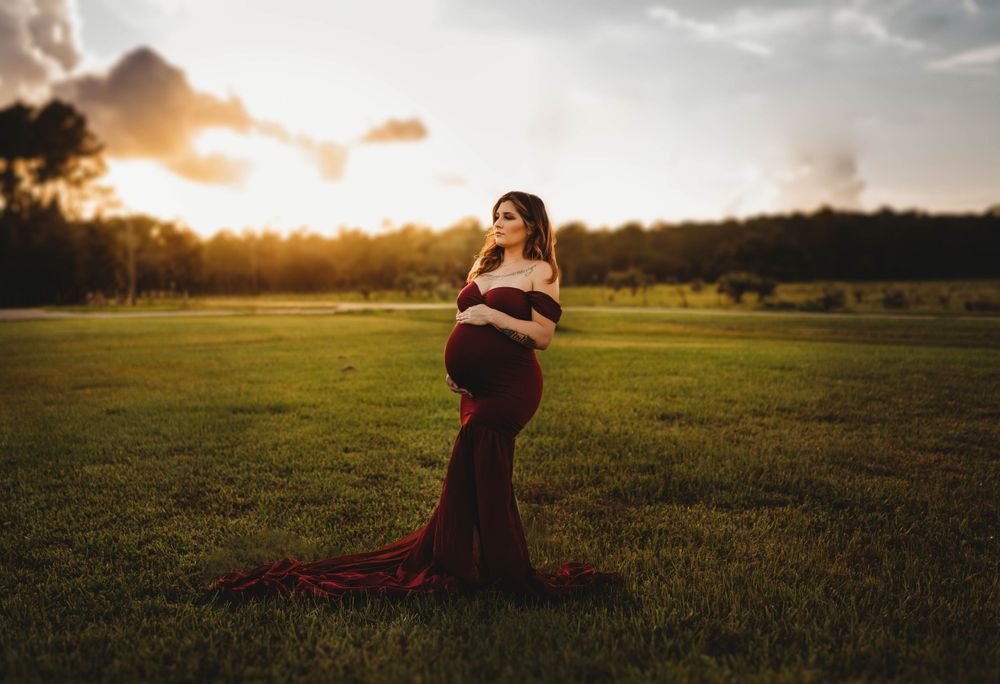 Silhouette of an expectant mother in a flowing burgundy dress against a golden sunset.