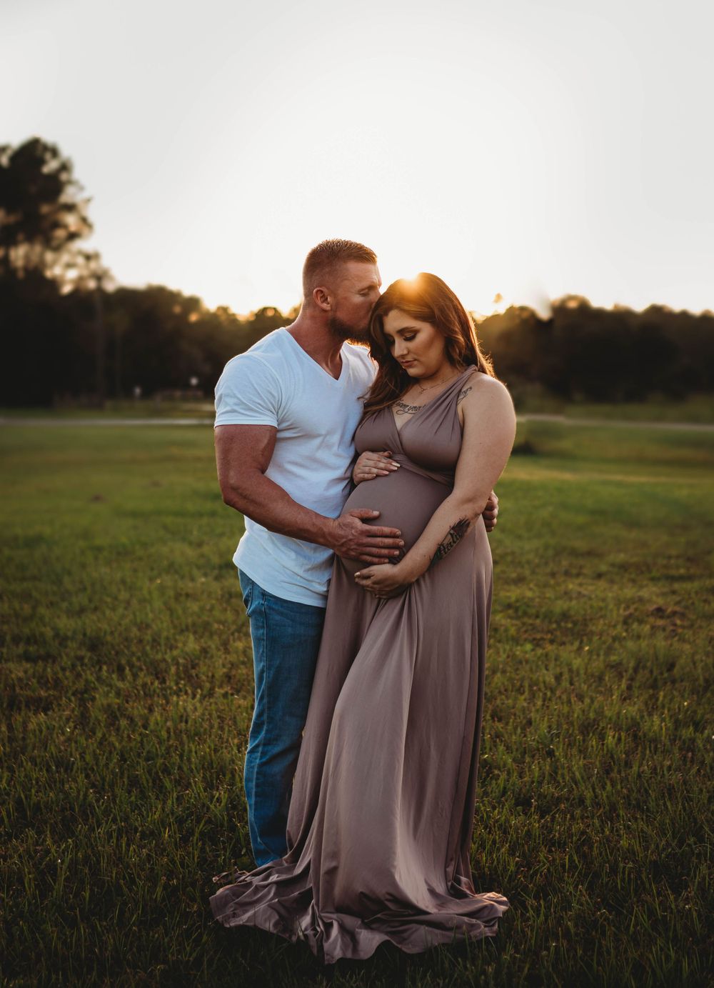Romantic sunset maternity photo of a couple embracing in a grassy field.