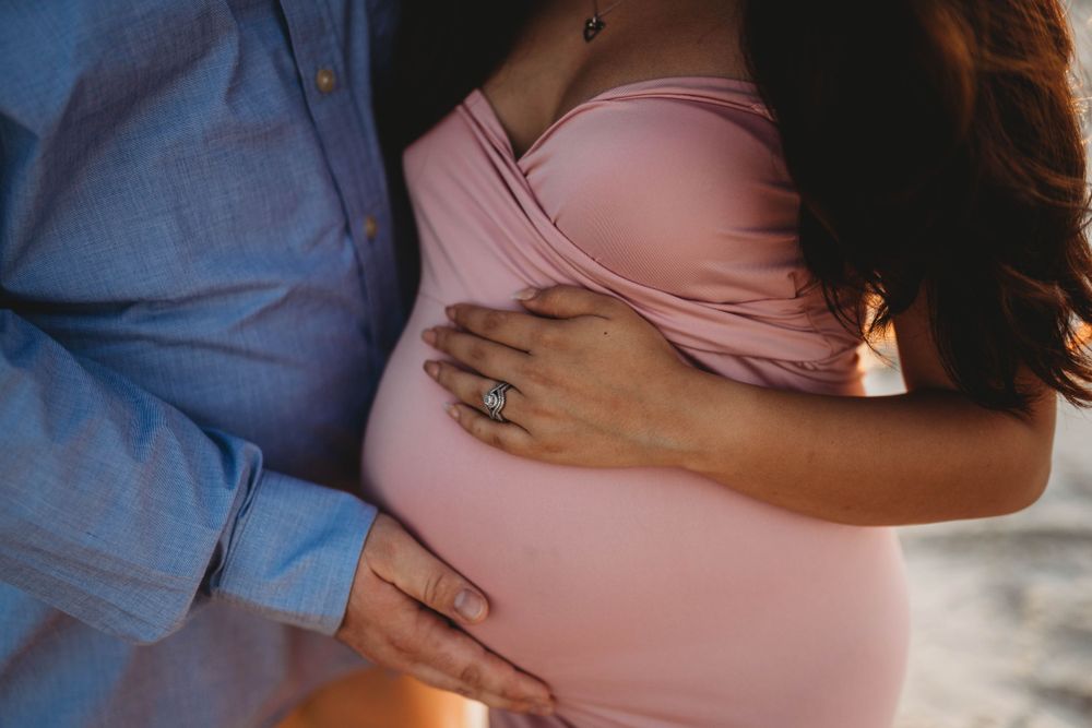 Close-up shot of hands cradling a pregnant belly in pink maternity dress.
