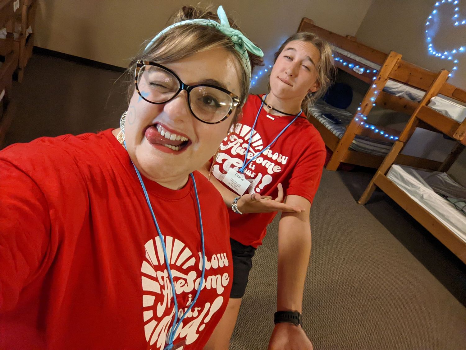 Two people in matching red t-shirts taking a selfie in what appears to be a dorm room.