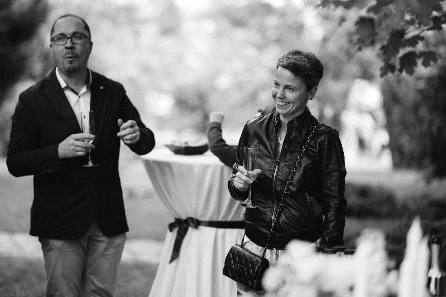 Black and white photo of guests enjoying drinks at outdoor wedding reception.