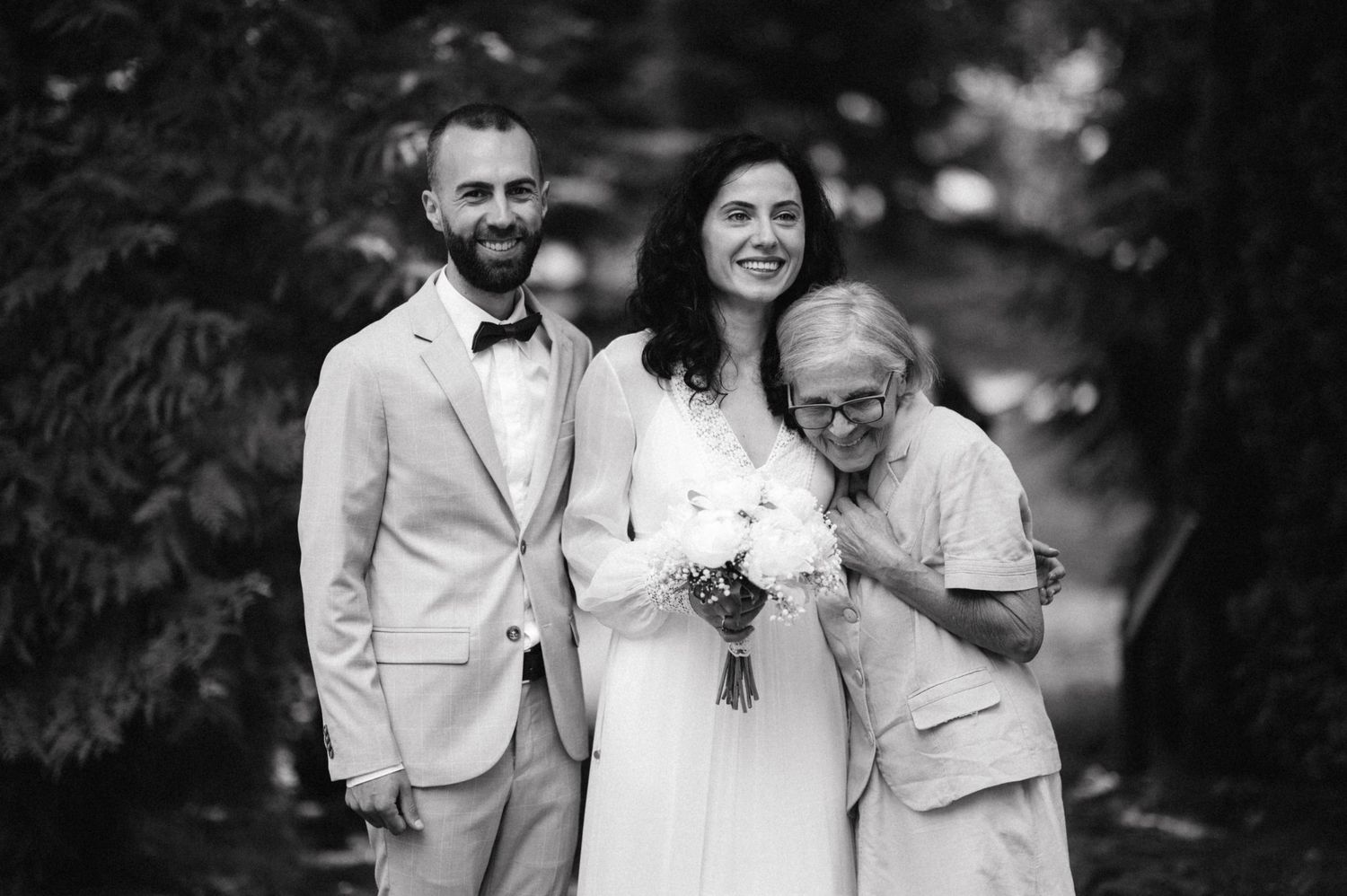 Black and white portrait of wedding couple with guest at outdoor garden reception.