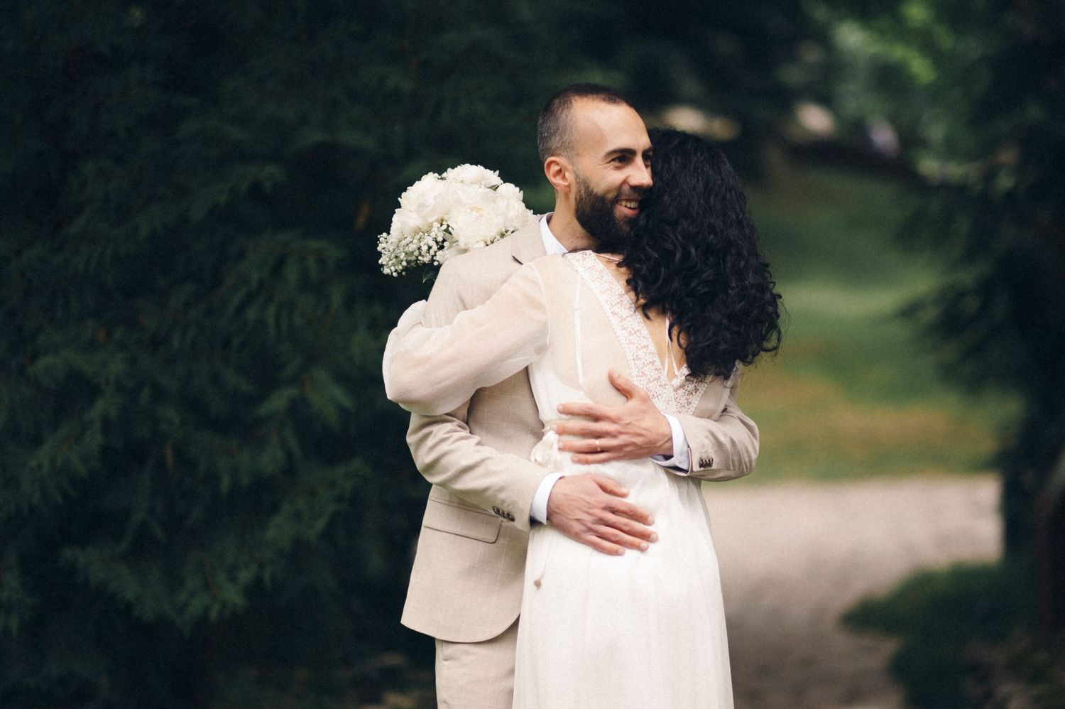 A tender embrace between a couple in wedding attire on a garden path.