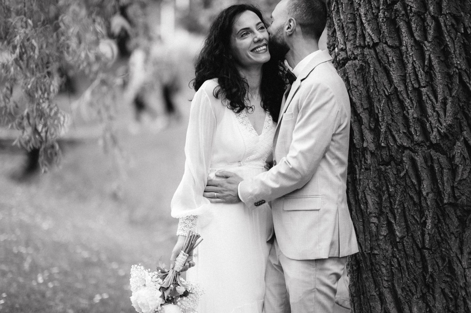 Black and white wedding photo of a couple sharing an intimate moment against a tree.