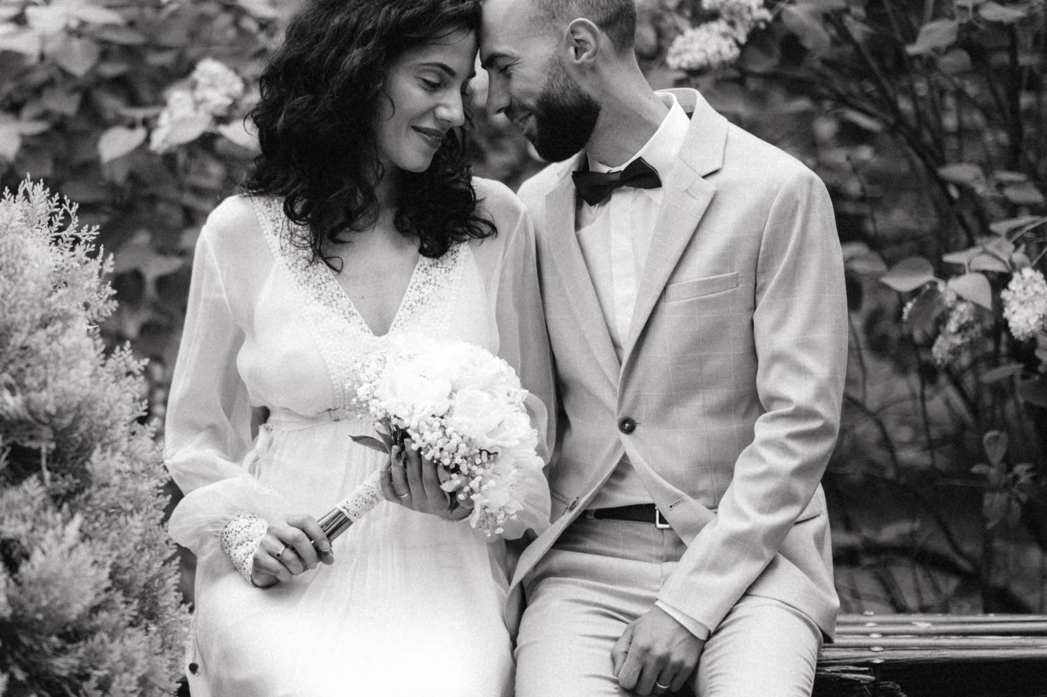 Black and white portrait of newlyweds sitting together with white bouquet.