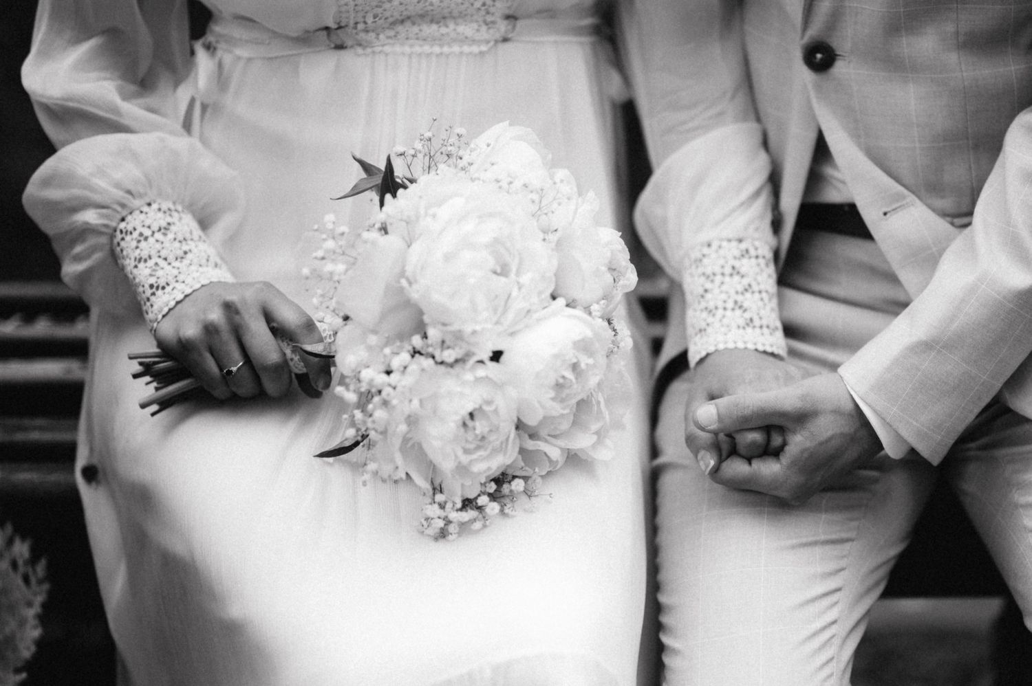 Black and white detail shot of wedding couple's hands and white floral bouquet.