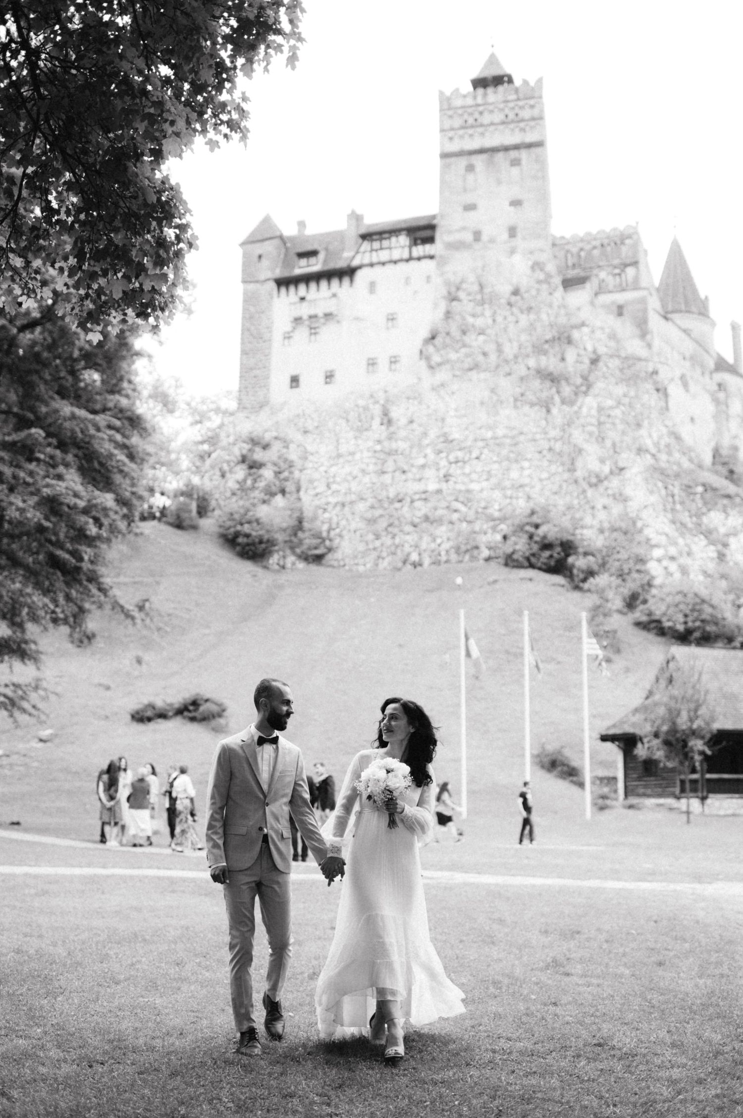 Wedding couple walks hand in hand with historic castle Bran in background.