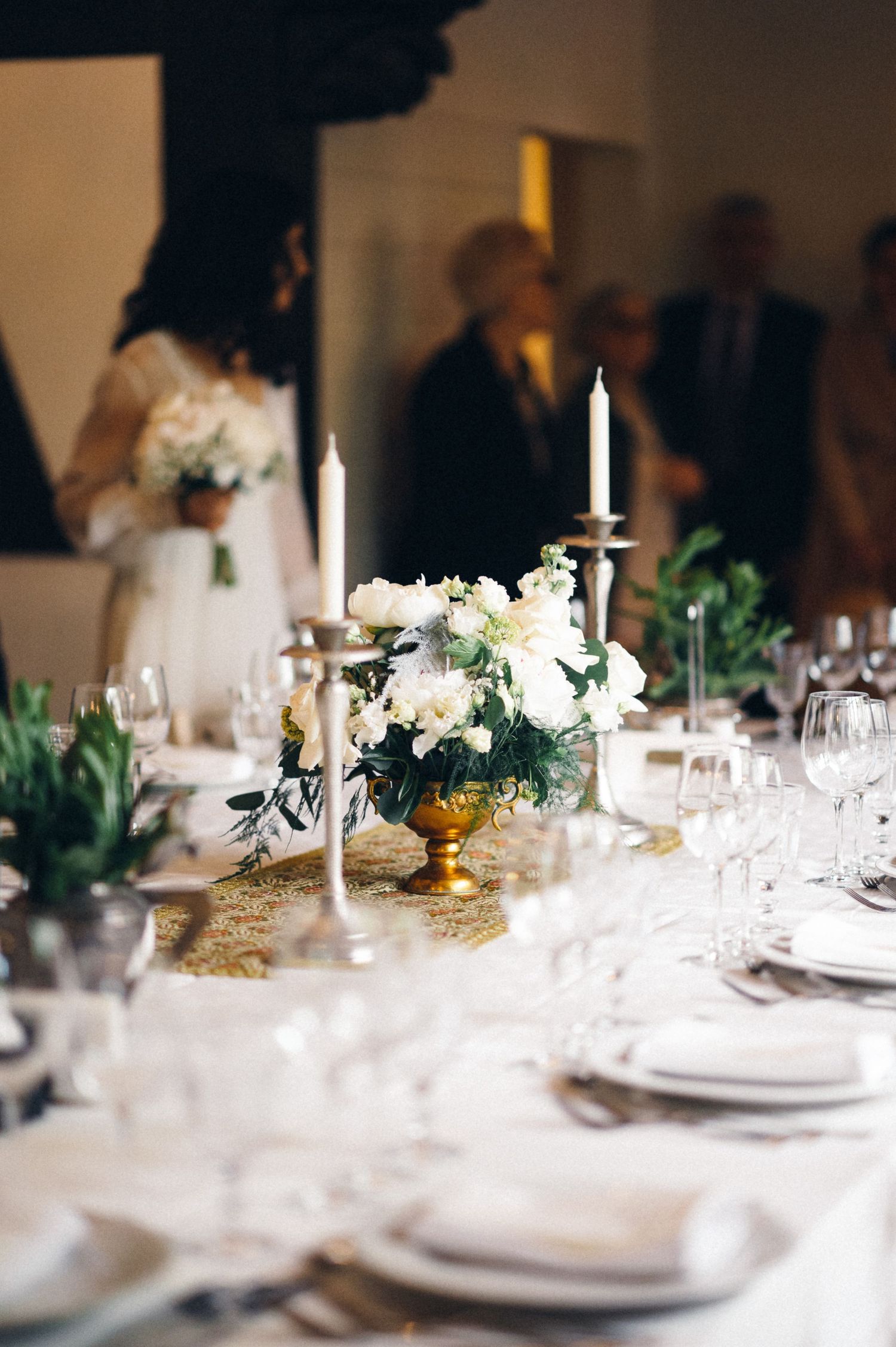 Elegant wedding reception table with white floral centerpiece, candles, and place settings.