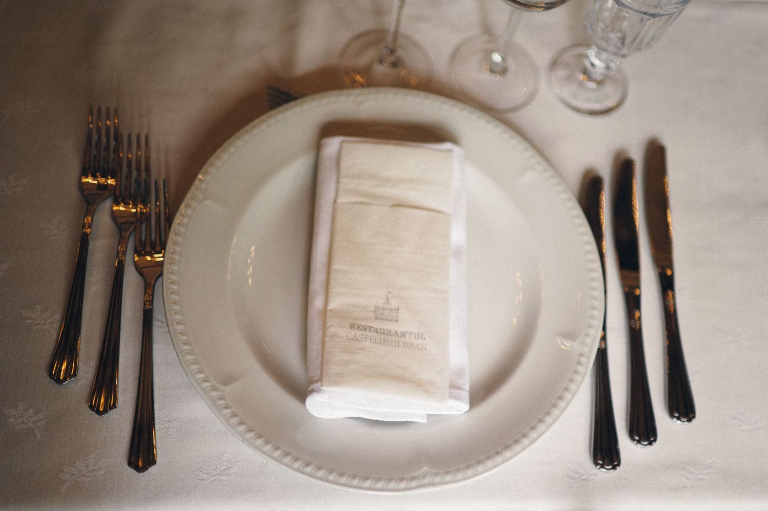 Formal place setting with white plate, folded napkin, and black silverware on white tablecloth.
