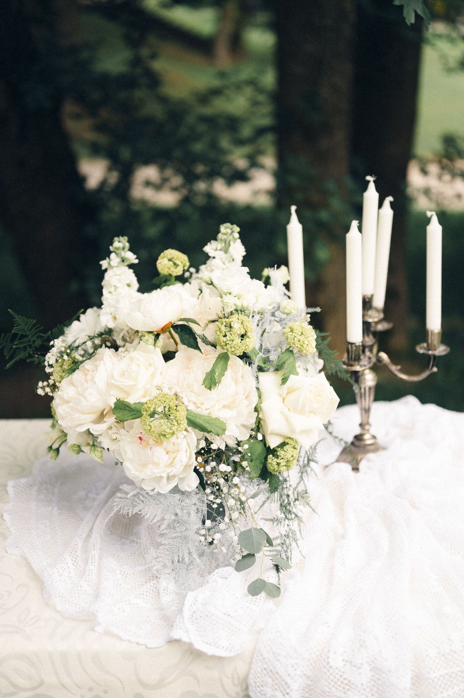 Elegant white floral centerpiece with candles on lace tablecloth for wedding reception.