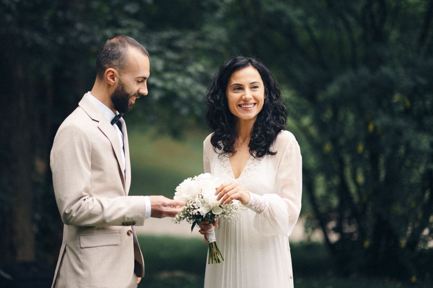 A tender moment during an outdoor wedding ceremony with a light beige suit and white dress.