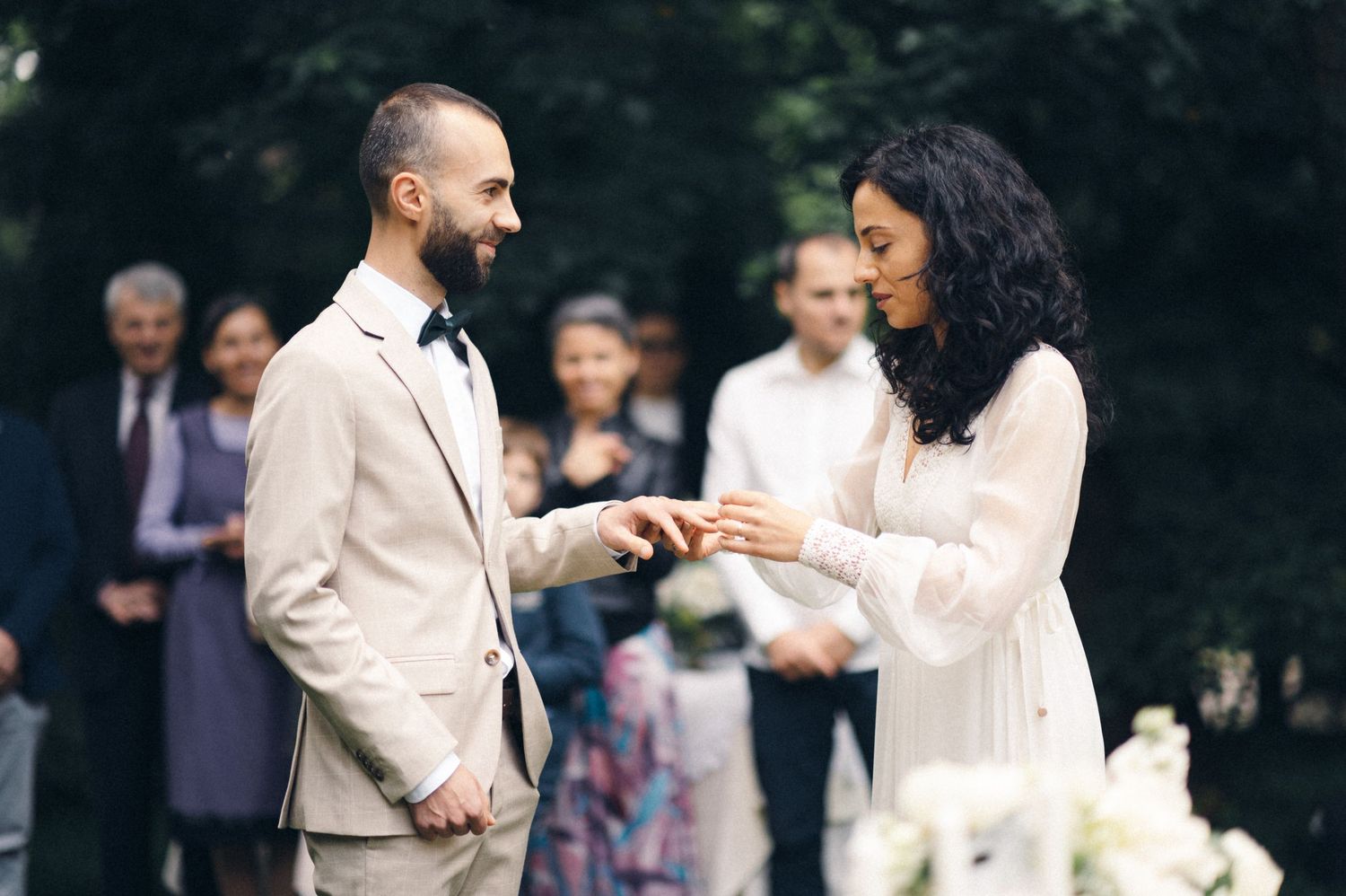 An exchange of rings during an intimate forest wedding ceremony with guests watching in background.