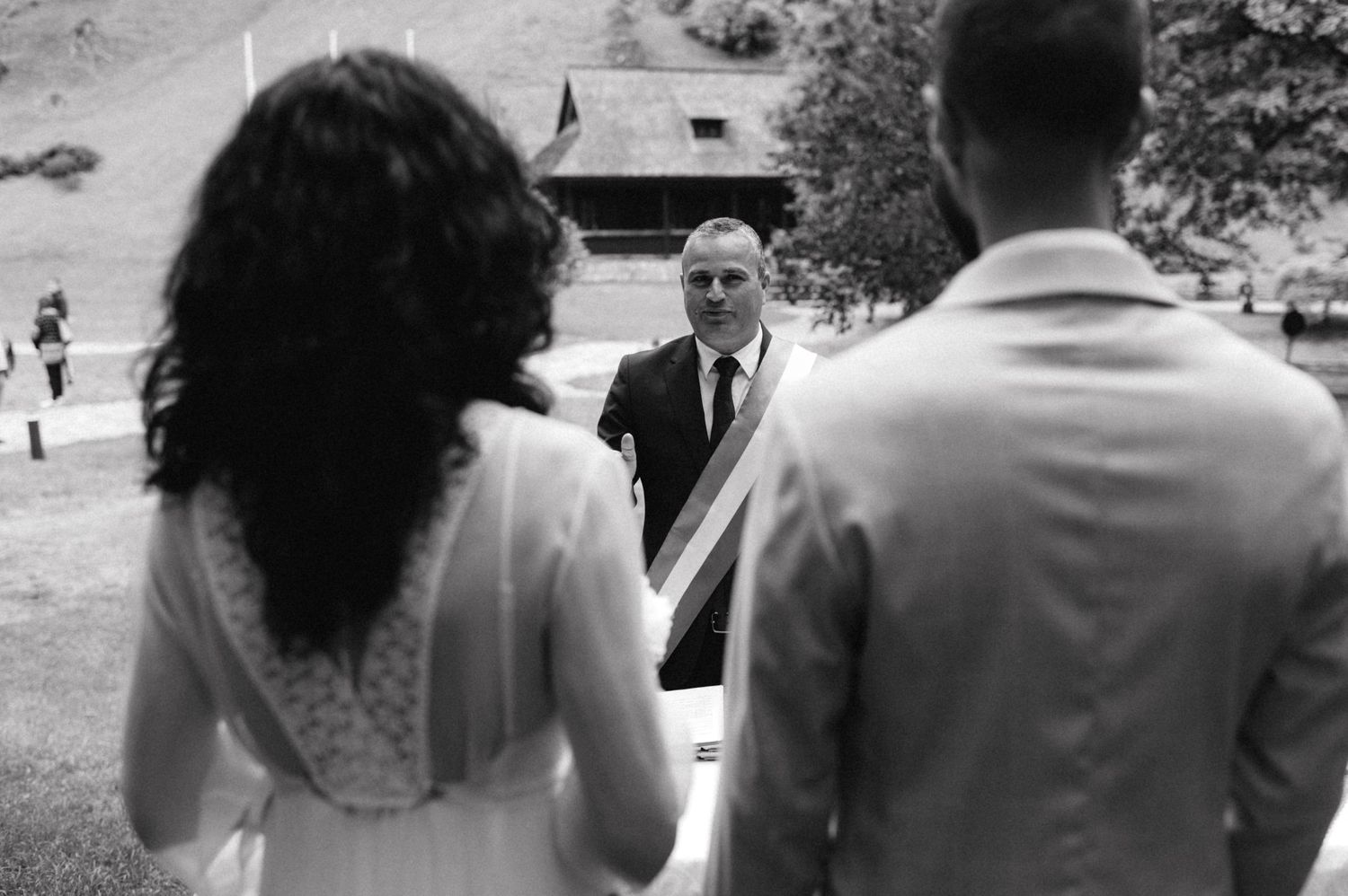 Black and white wedding ceremony scene showing couple from behind with officiant in foreground.