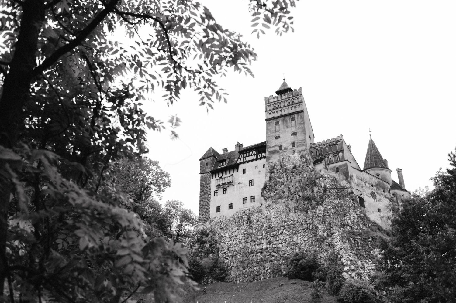 Black and white photograph of historic Bran Castle perched on hilltop in Romania.