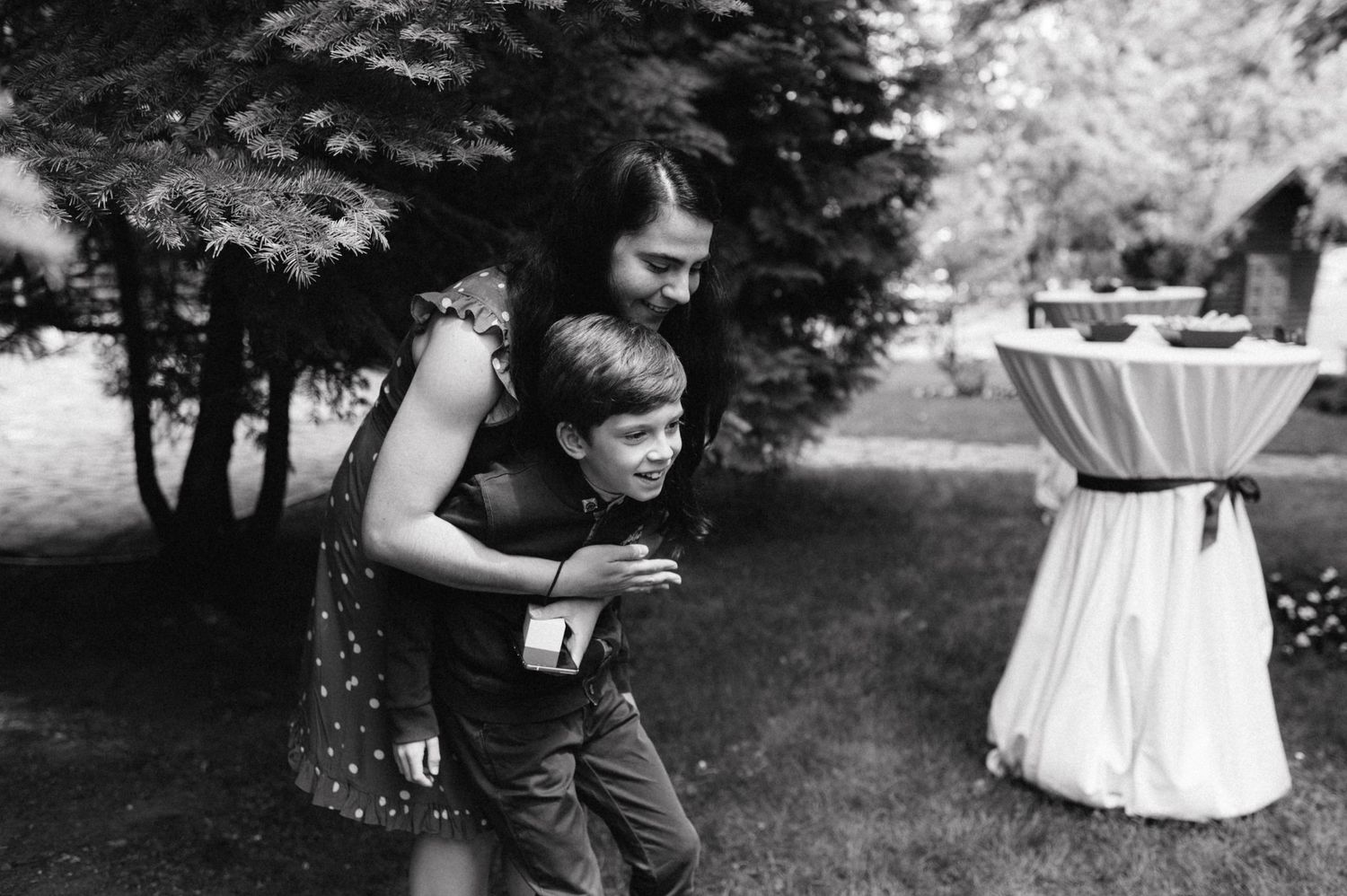 Black and white candid moment at outdoor wedding reception with cocktail table in background.