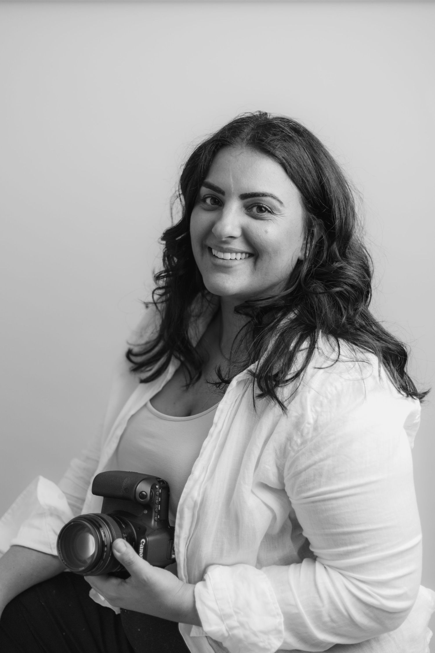 Black and white portrait of photographer holding camera in casual studio setting.