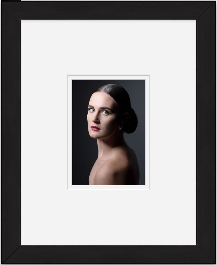 Elegant studio portrait with dramatic lighting and classic bun hairstyle in a black frame.
