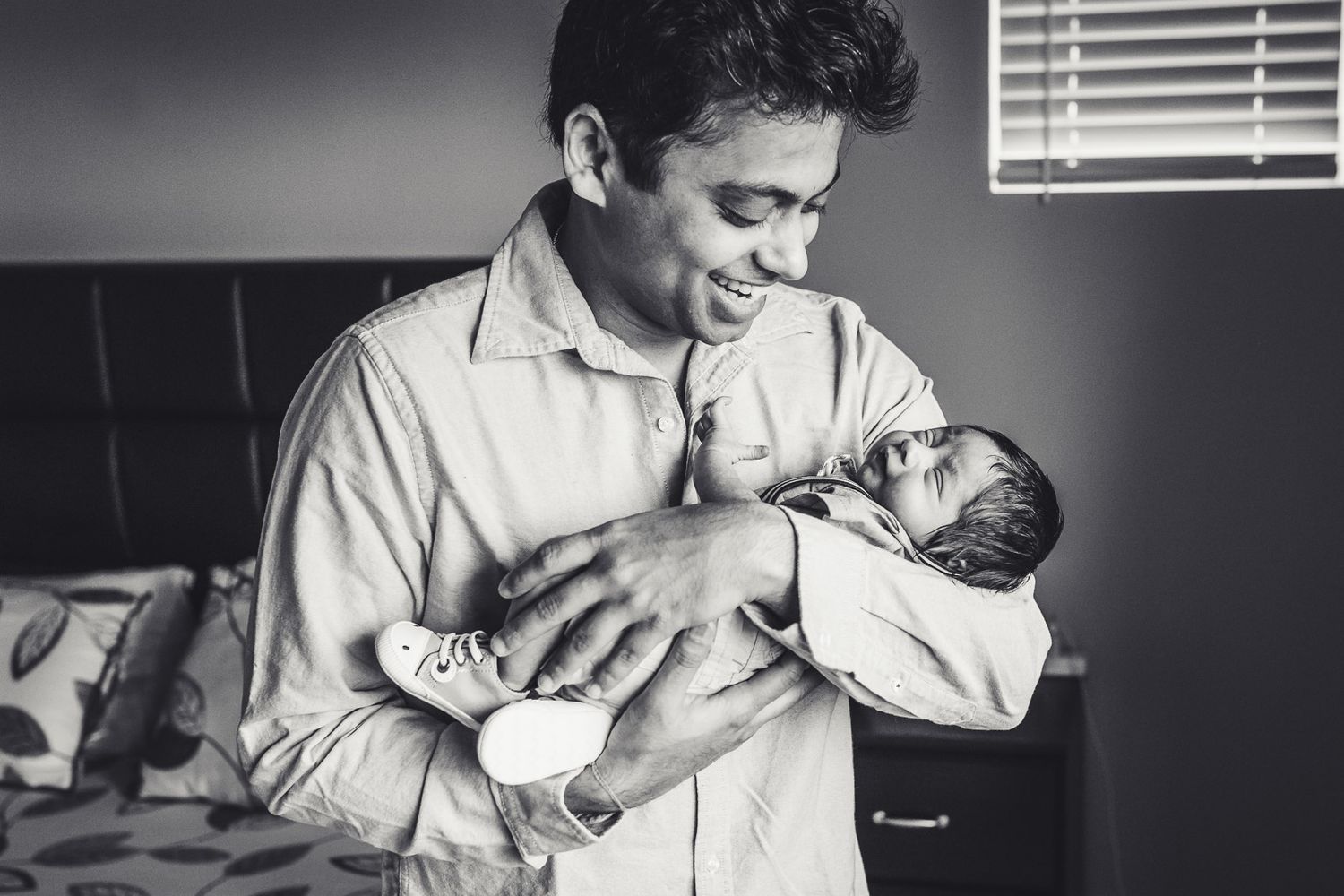 Black and white photo of father smiling and holding newborn son at home in Seattle.
