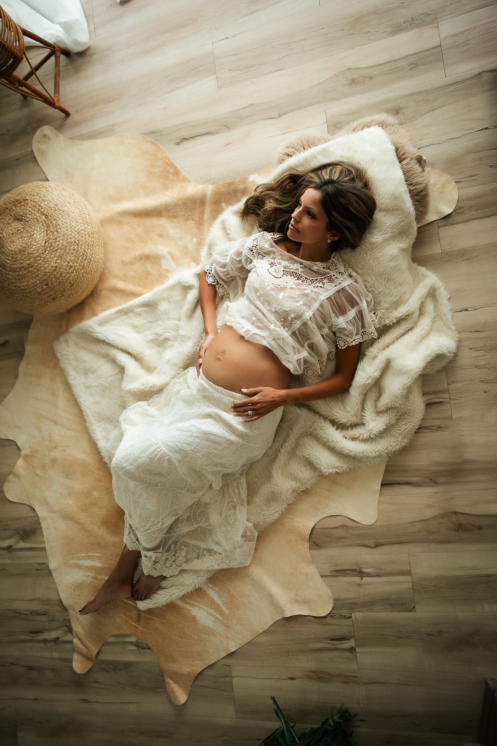 Overhead view of maternity portrait on white fur rug with lace dress and wooden floor.