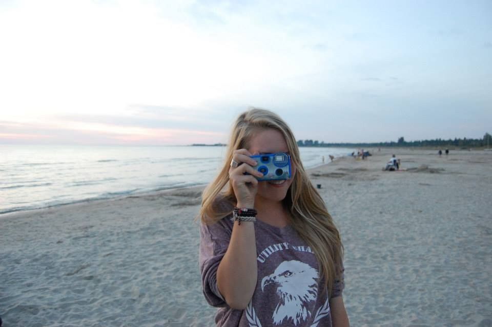 Photographer in a graphic t-shirt taking a photo at sunset on a beach with mirrored sunglasses.