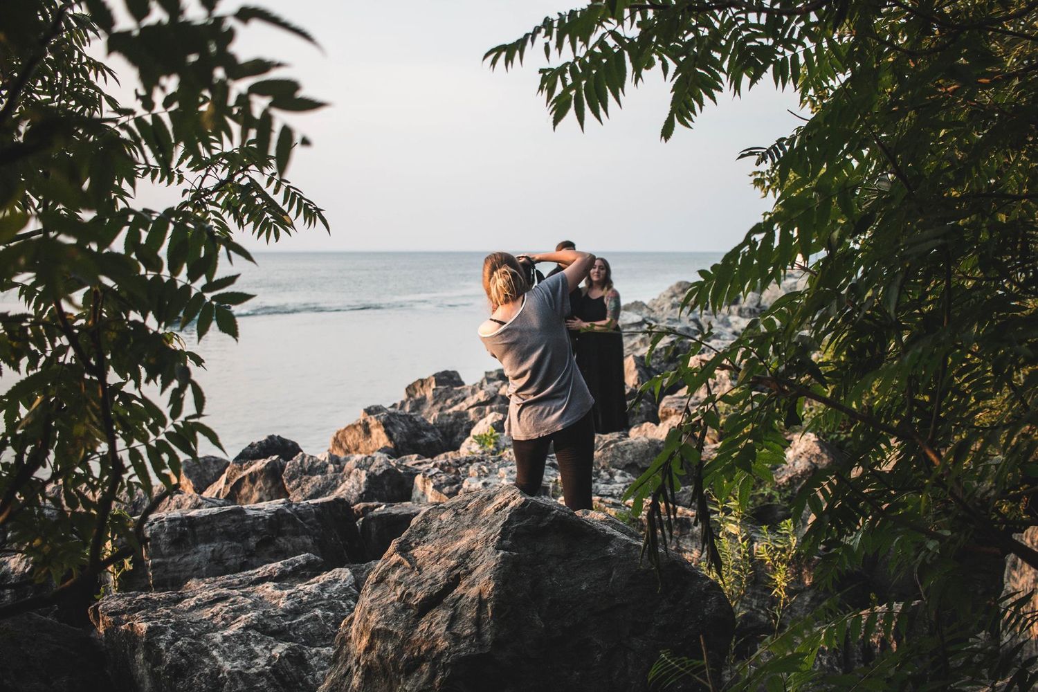 Photographers capturing sunset photos on rocky coastal outcrop surrounded by trees.