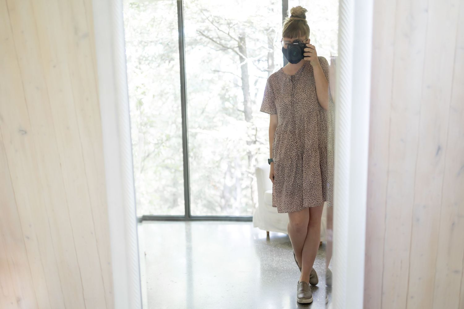Photographer taking self portrait in minimalist white hallway.