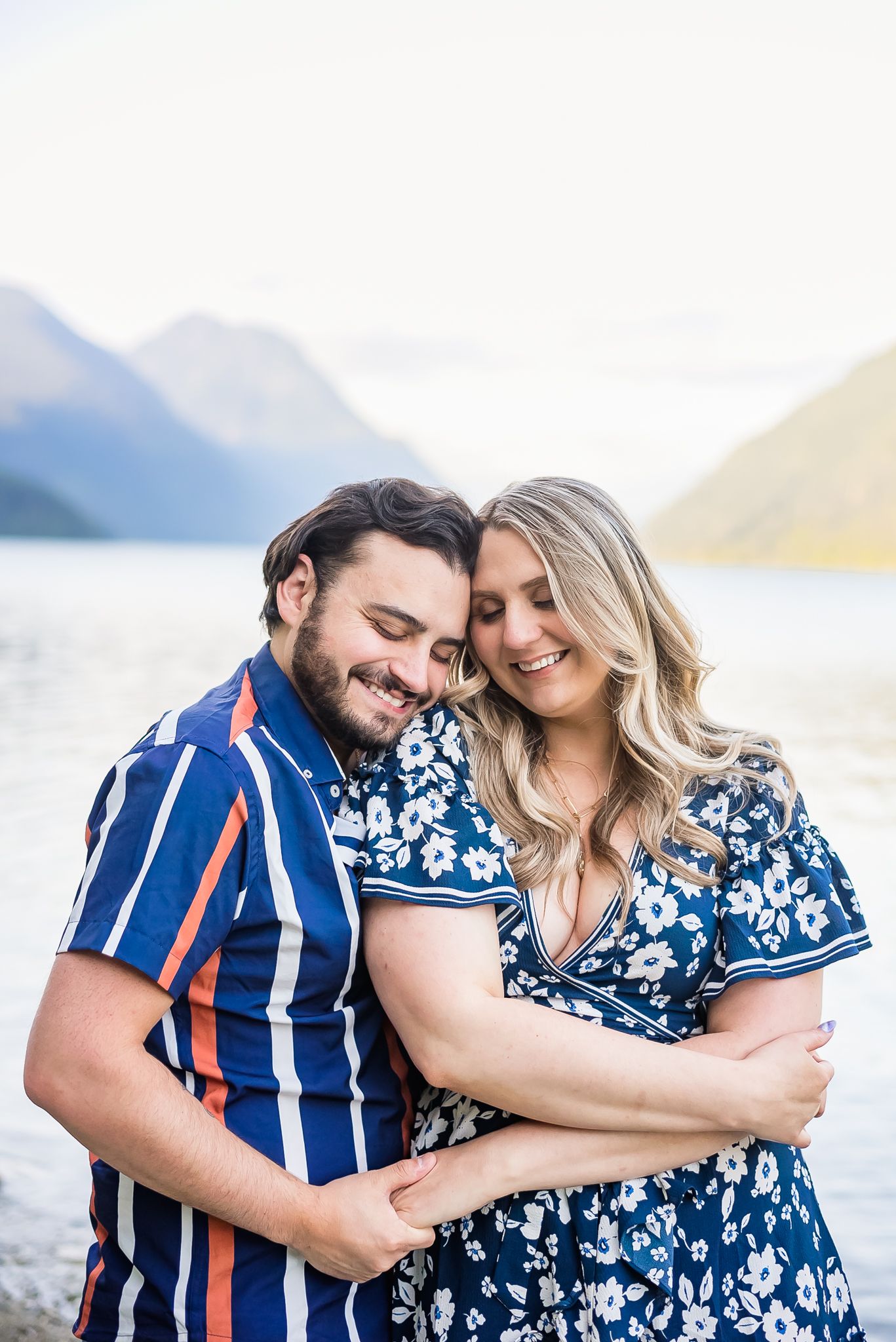 At Golden Ears Park in Maple Ridge, a couple hold each other close and smile with the lake and mountains in the background.