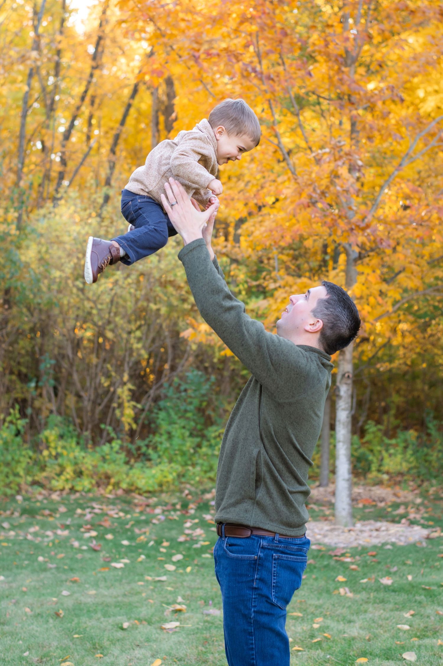 A playful moment captured in autumn as a small child is lifted high against a background of golden fall foliage.
