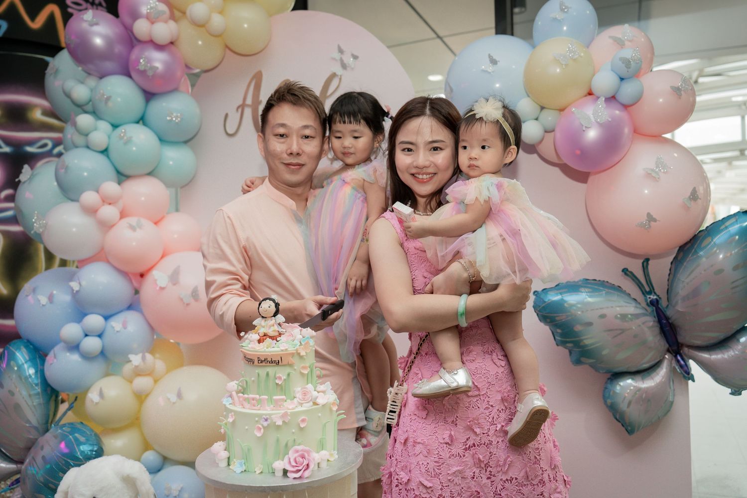 Family celebration with pastel balloon arch and decorated cake.