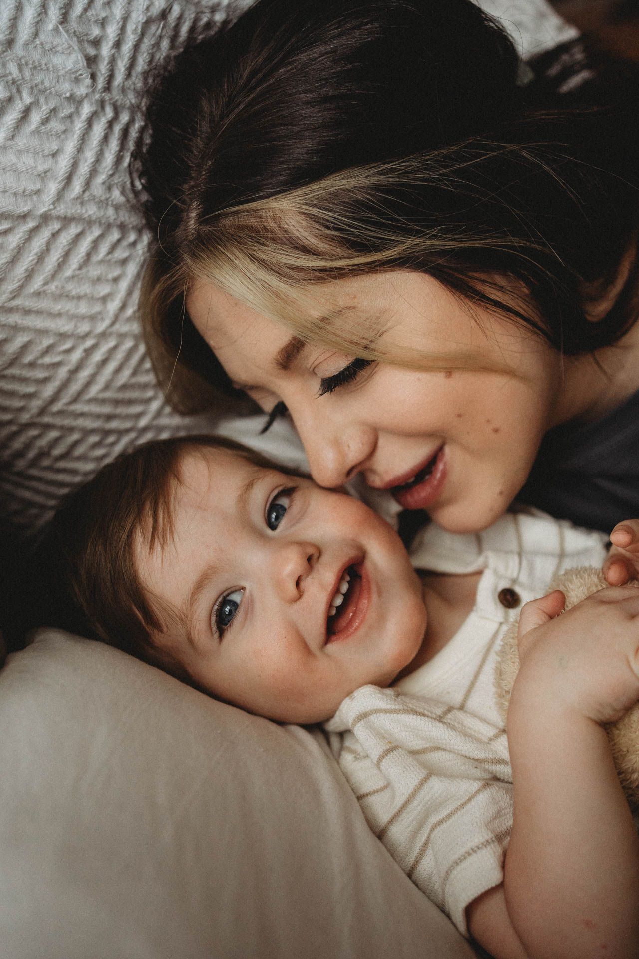 A heartwarming moment between parent and child cuddling and laughing together on soft bedding.