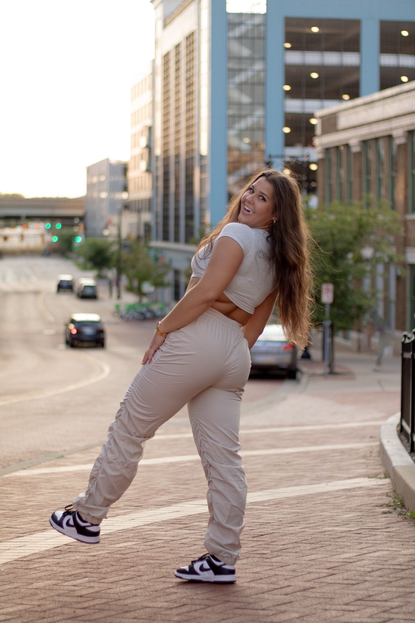 Casual street fashion photo of someone in a slouchy beige jumpsuit and sneakers posing against an urban backdrop.