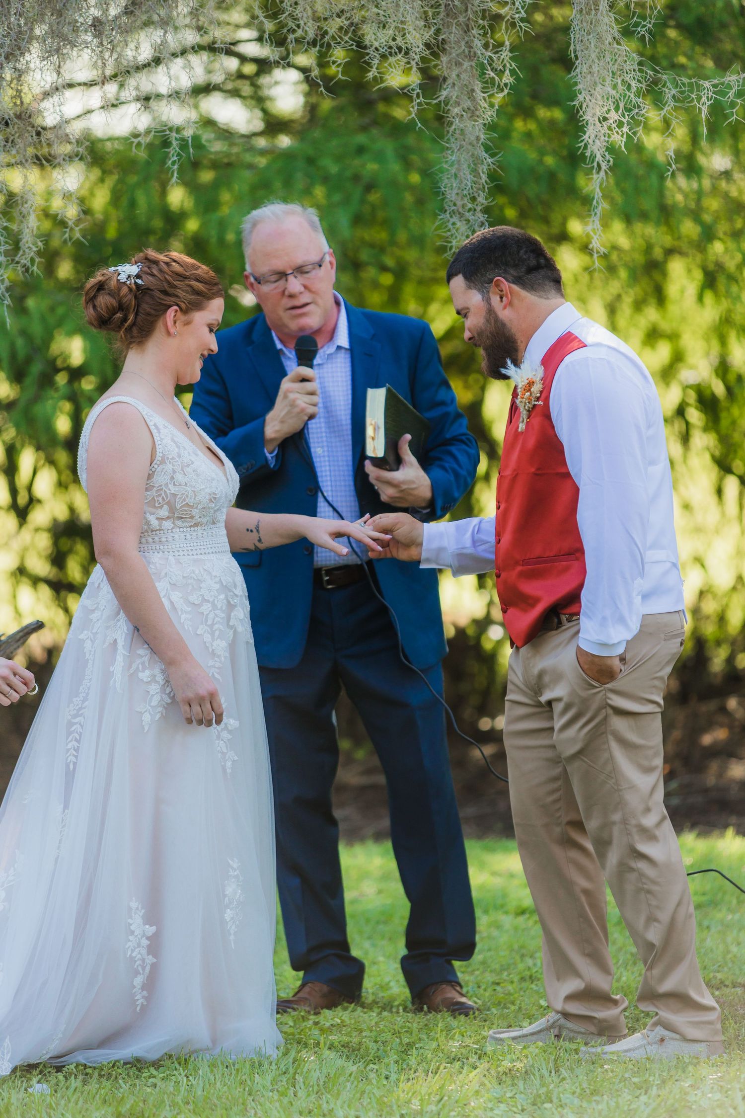 An outdoor wedding ceremony under mossy trees with the officiant speaking to the couple.
