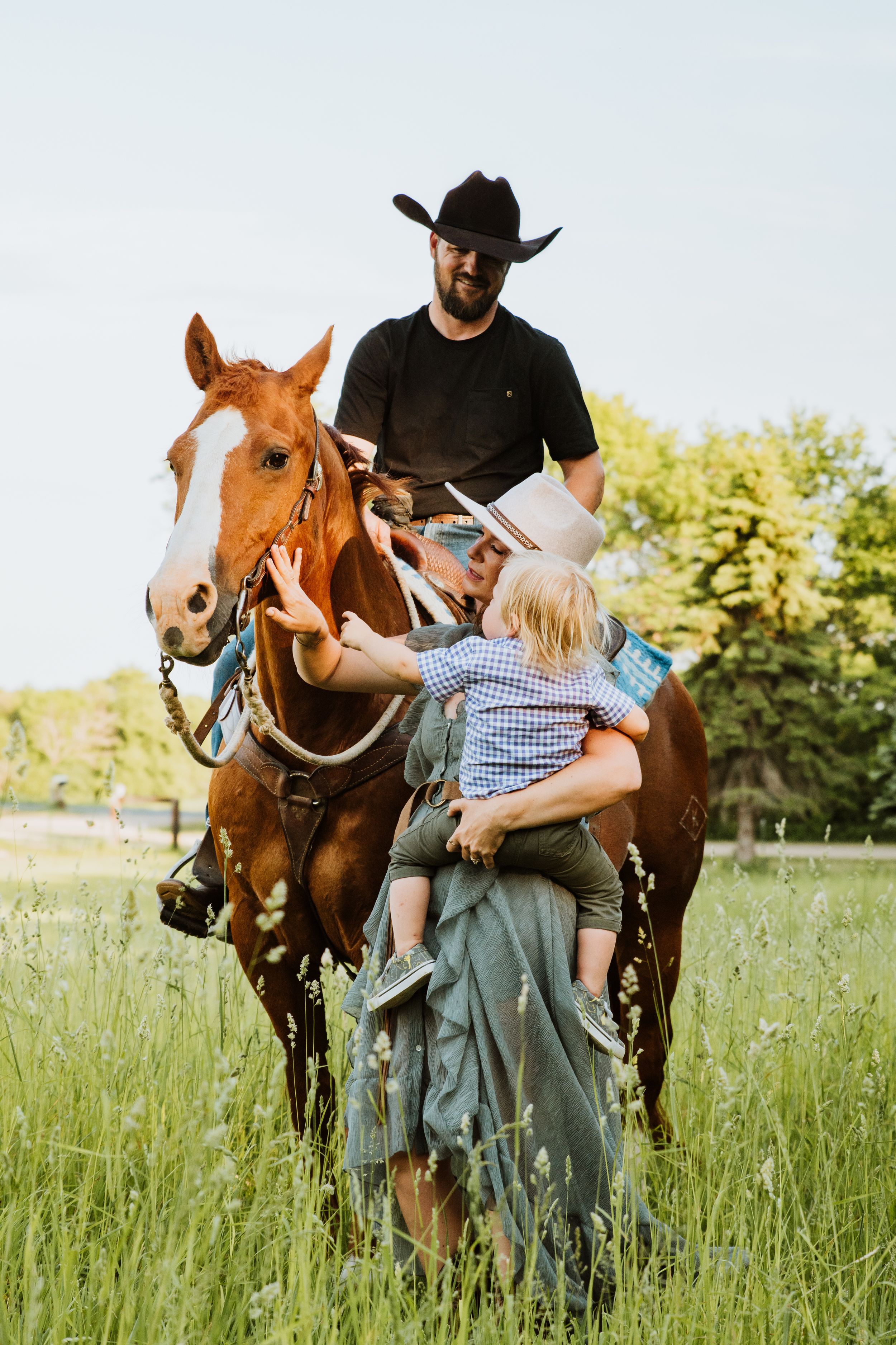 Family poses with horses in a tall grass meadow during a summer photo session.