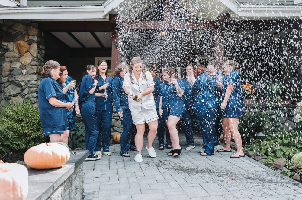 Wedding party celebrates with confetti in front of stone building with blue attire and pumpkin decor.