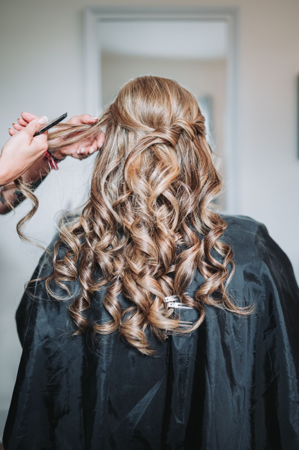 Styled blonde curls being arranged during a wedding day hair preparation session.