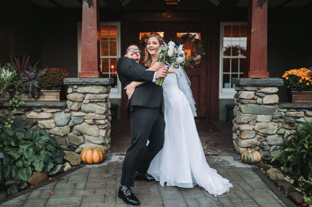 A joyful wedding moment in front of a rustic stone and wood entrance with fall pumpkin decor.