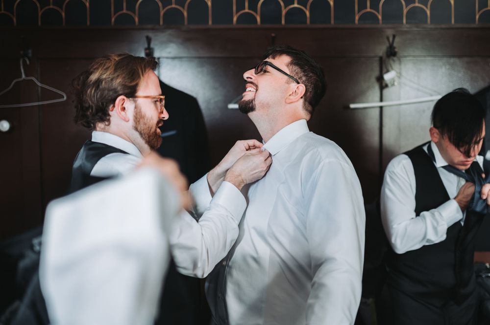 Two people share a lighthearted moment while adjusting formal attire before an event.