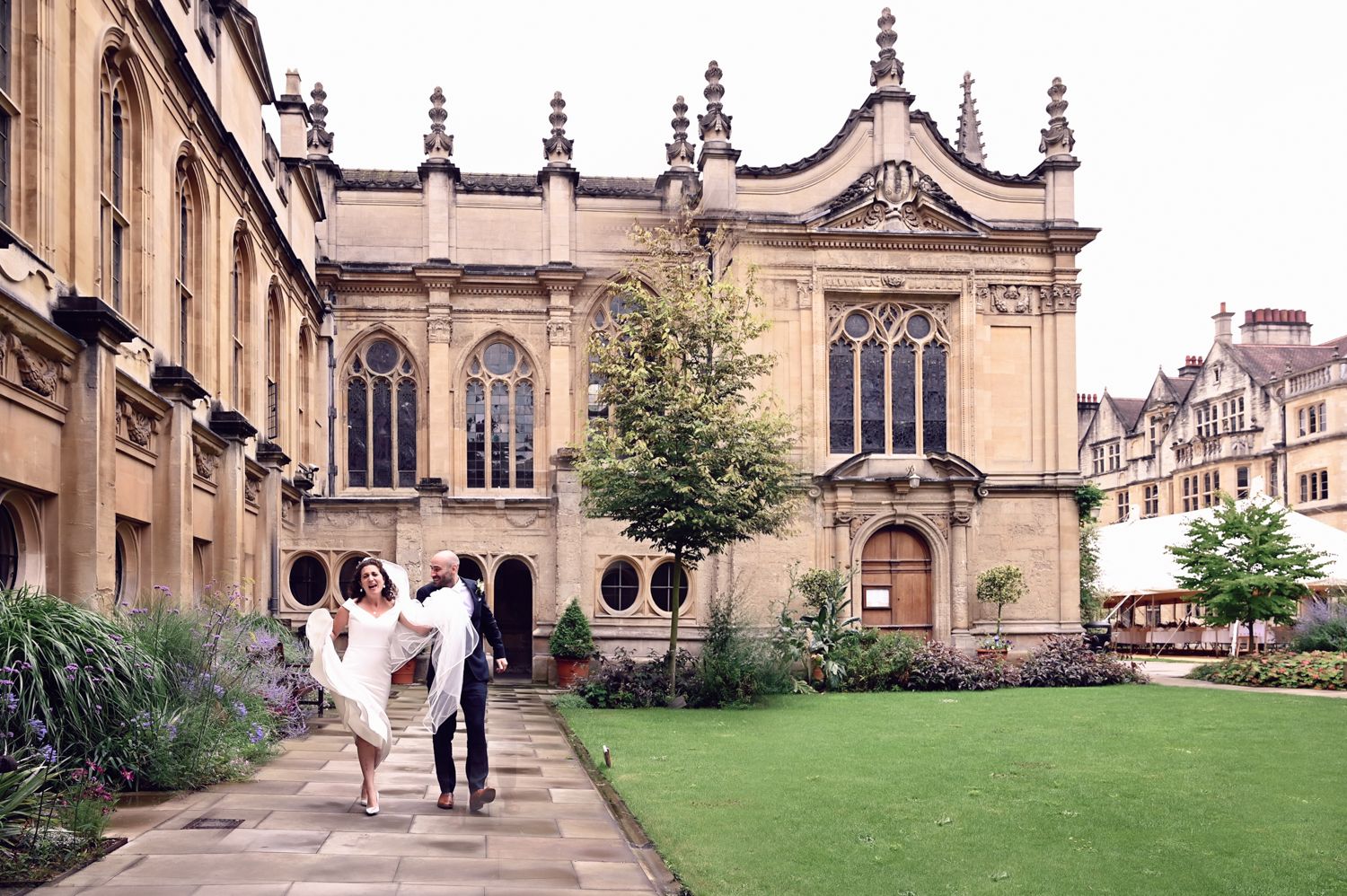 Couple walking along path by Gothic architecture building with manicured lawn.