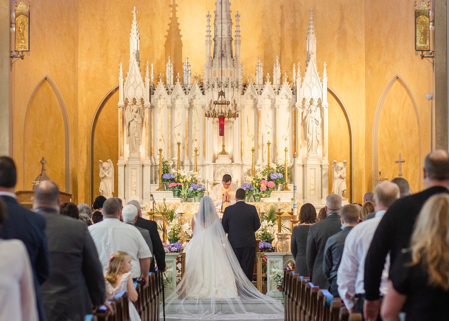 Traditional Catholic church wedding ceremony with ornate Gothic altar and stained glass windows.