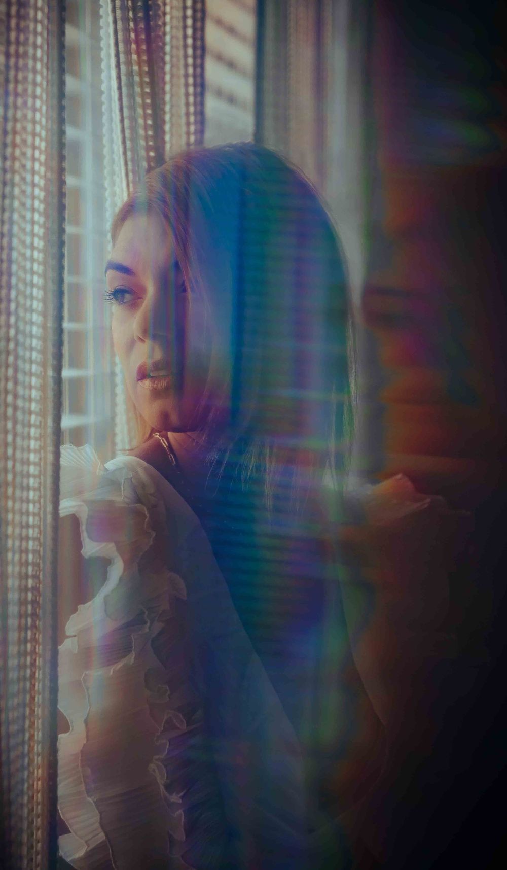Ethereal portrait with rainbow prism effects and soft reflective lighting through glass.