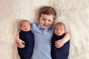 Three siblings posed together on white fluffy rug for professional portrait.