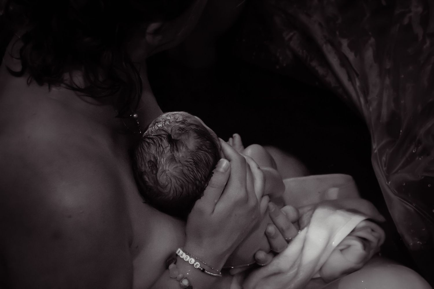 Black and white image of a mother holding her newborn baby to her chest in a birthing tub.