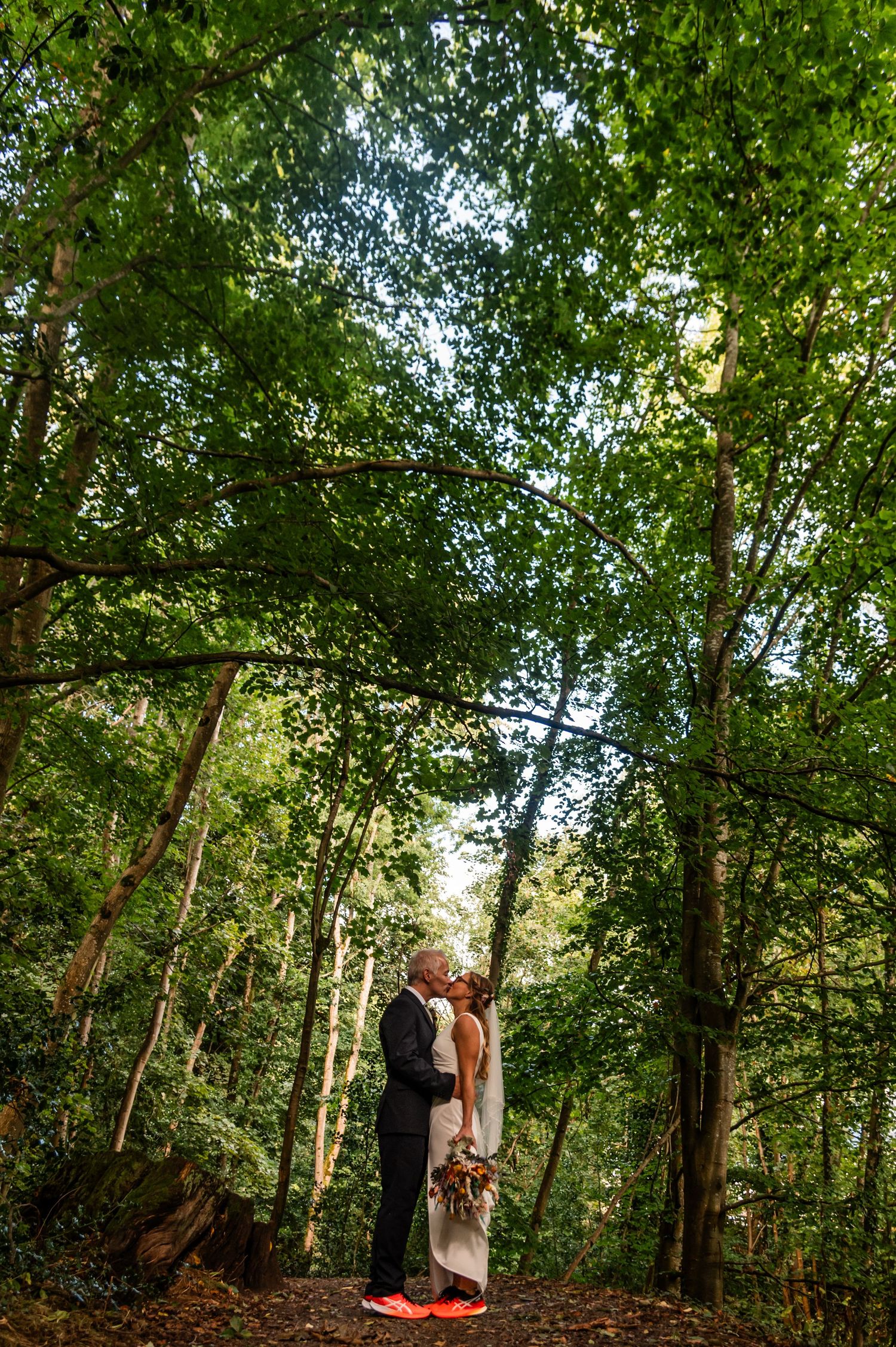 Wedding portrait framed by tall trees in a lush green forest setting.