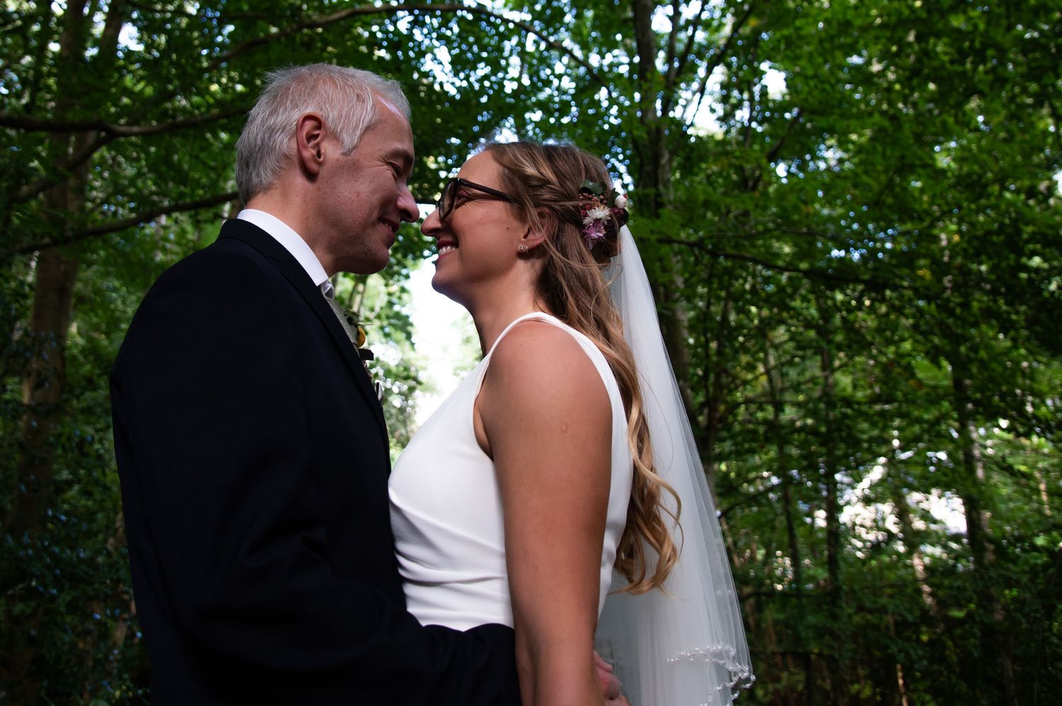 Wedding couple shares intimate moment on garden bridge with natural foliage backdrop.