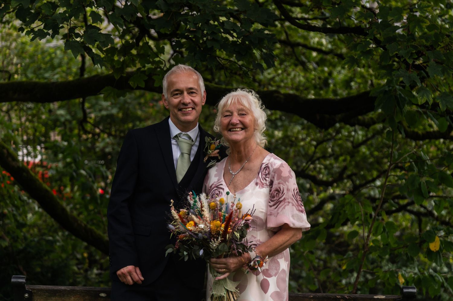 Wedding party celebrates on a green lawn with natural foliage backdrop.