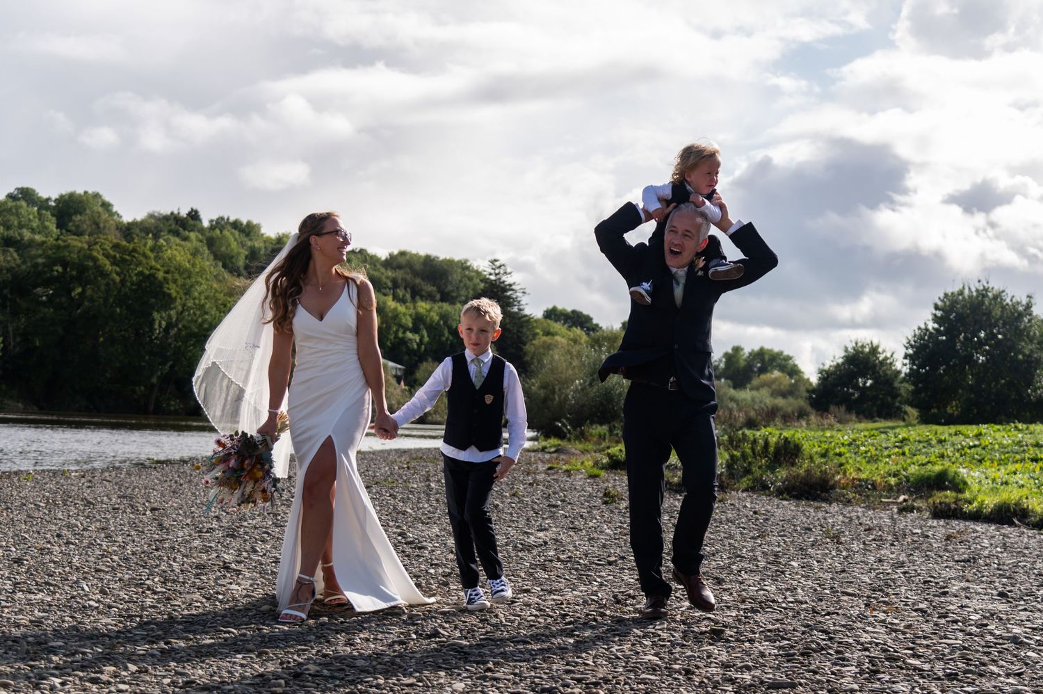 Playful wedding photoshoot on rocky beach with dramatic cloudy sky.