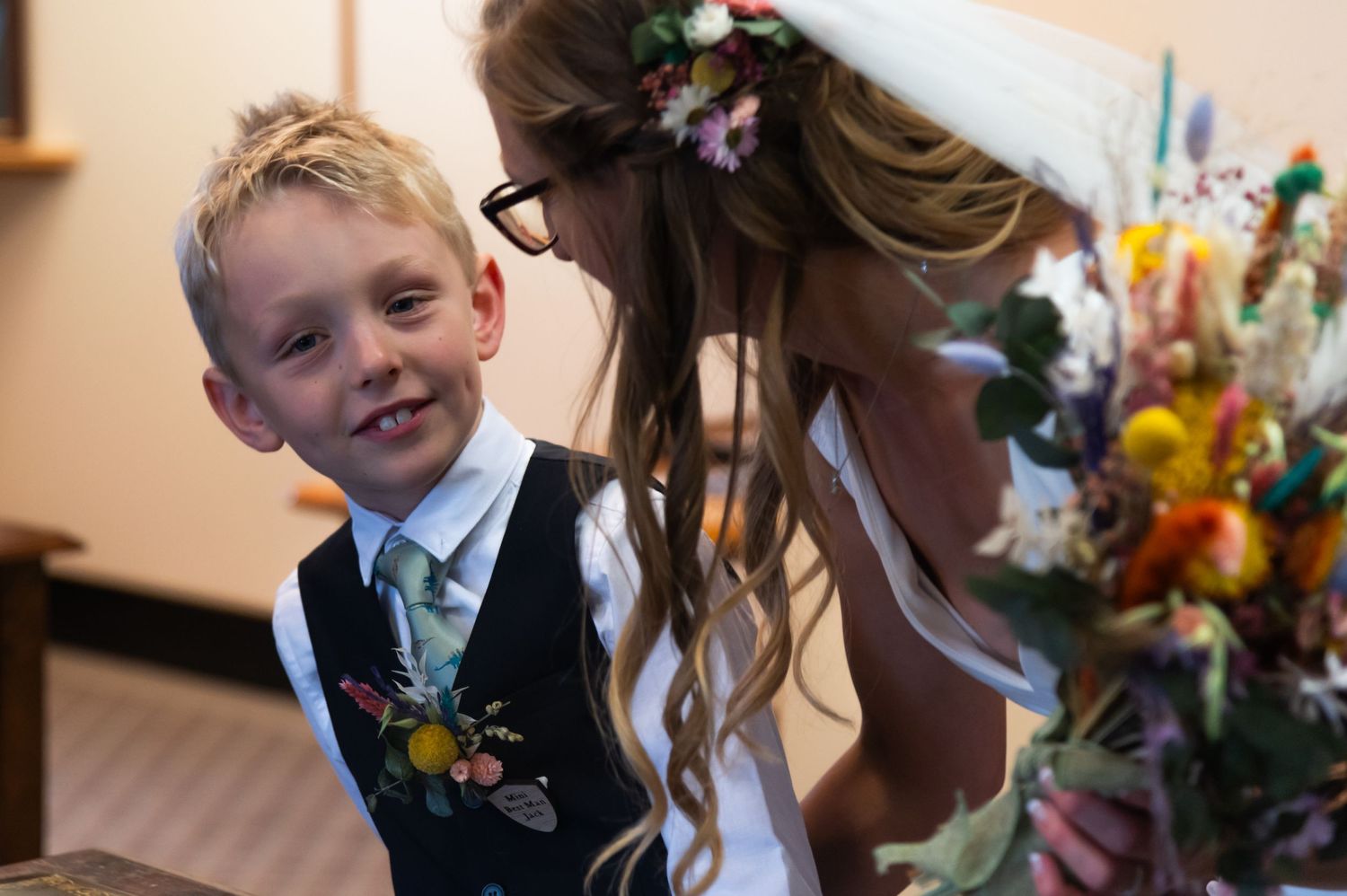 A young child in formal attire smiles during wedding festivities.