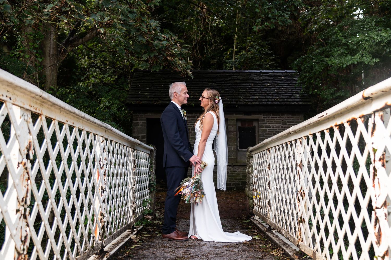 A couple poses on a white lattice bridge during their wedding day.