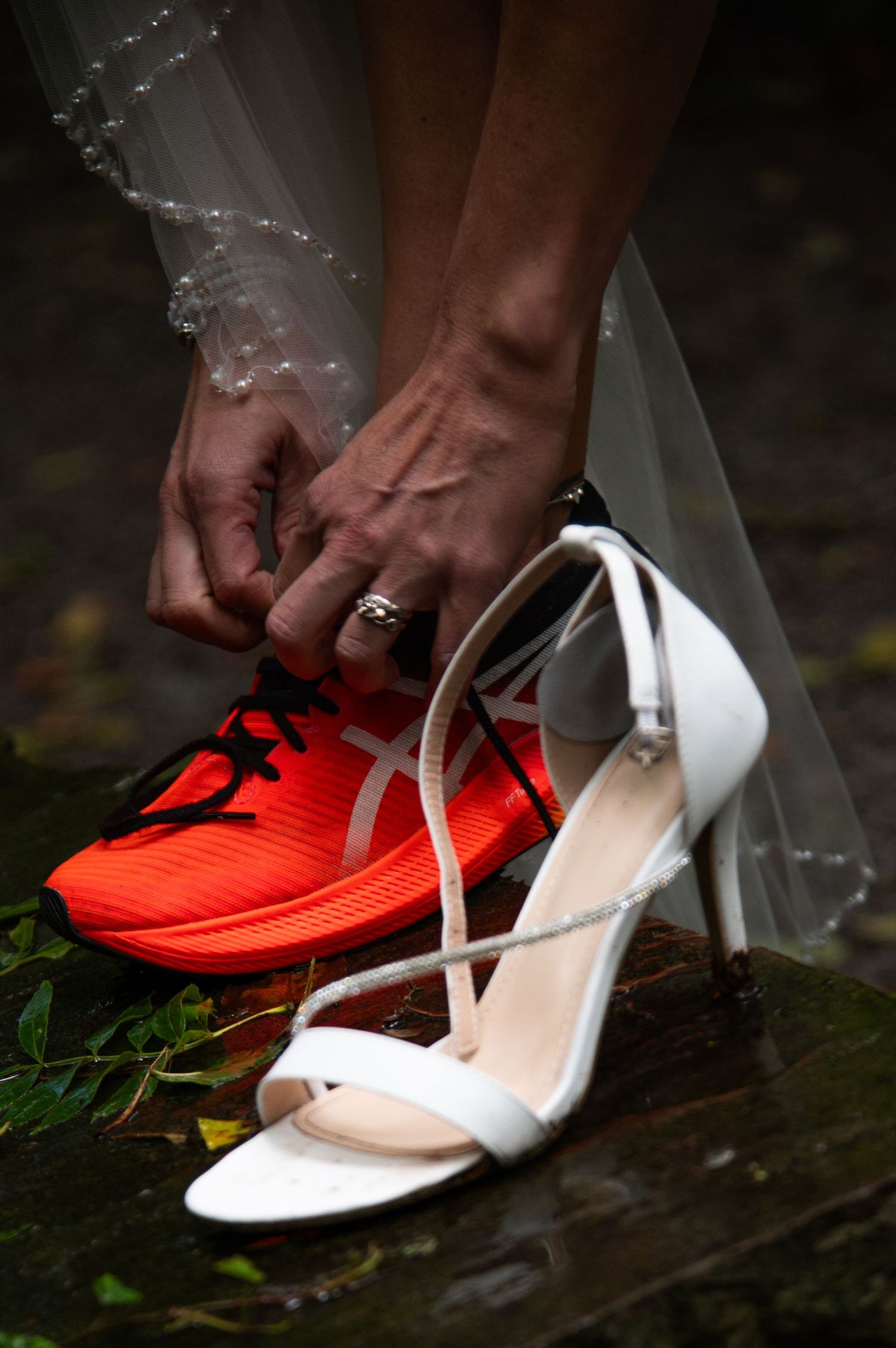 Wedding shoes detail shot showing white heels and bright red sneakers on stone.