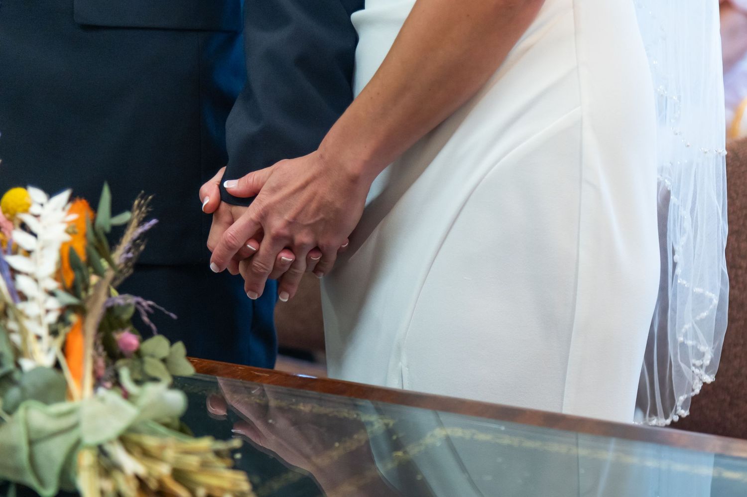 Close-up details of a bride's white wedding dress against dark suit.
